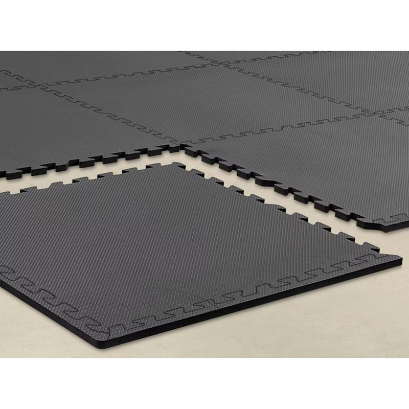 Two black interlocking foam floor tiles partly joined on a pale floor, showing how the puzzle edges lock together