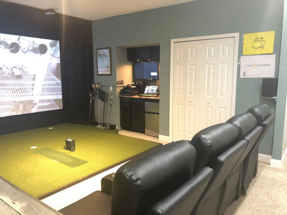 Basement golf simulator lounge with a projector screen, hitting turf and leather theater seats