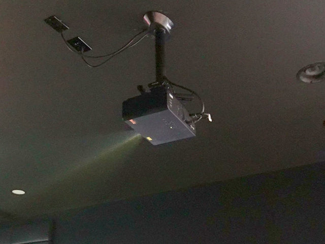 Ceiling-mounted golf simulator projector on its mount, beam lit